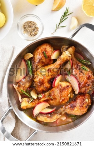 Chicken drumsticks baked with apples and herbs in pan. White background, top view, flat lay