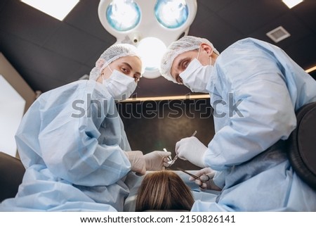 Surgeon performing cosmetic surgery on breasts in hospital operating room. Surgeon in mask wearing surgical loupes during medical procedure. Breast augmentation, enlargement, enhancement