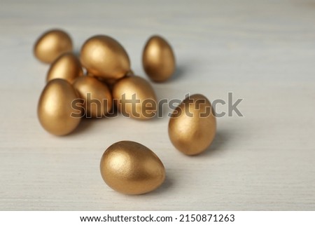 Shiny golden eggs on white wooden table