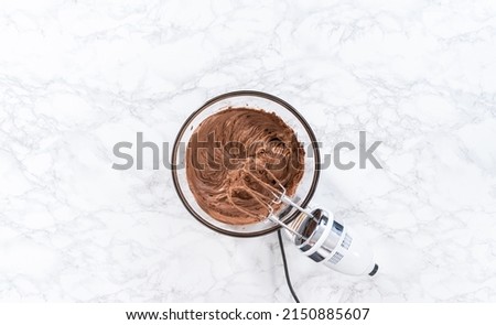 Flat lay. Mixing store-bought chocolate frosting in a mixing glass bowl with a hand mixer. Royalty-Free Stock Photo #2150885607