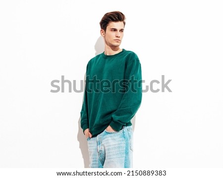 Portrait of handsome confident stylish hipster lambersexual model.Man dressed in green sweater and jeans. Fashion male posing in studio near white wall. Isolated Royalty-Free Stock Photo #2150889383