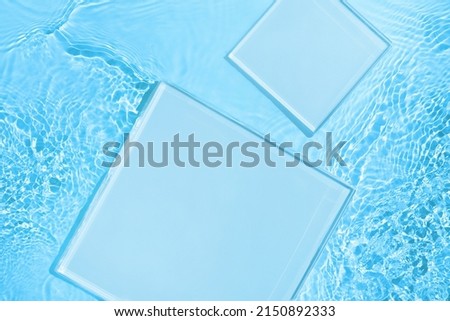 Two empty clear glass square podiums on blue transparent calm water texture with waves in sunlight. Abstract nature background for product presentation. Flat lay cosmetic mockup, copy space.
