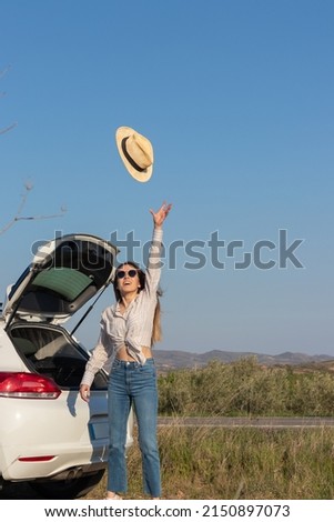 Vertical picture of teenager on sunglasses having fun throwing her straw summer hat in the air while in a road trip