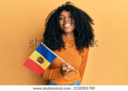 African american woman with afro hair holding moldova flag looking positive and happy standing and smiling with a confident smile showing teeth 