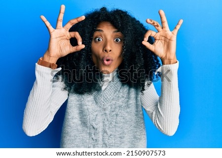 African american woman with afro hair wearing casual winter sweater looking surprised and shocked doing ok approval symbol with fingers. crazy expression 