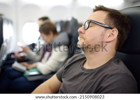 Mature man sleeping while traveling by an airplane. Tired passenger napping during flying in aircraft. Long-haul flights. Royalty-Free Stock Photo #2150908023