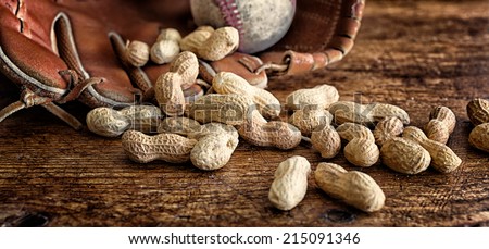 Roasted peanuts in the shell on rustic wood. Baseball and glove in the background. Banner format and rich vintage color. Concepts: snacks, baseball, nostalgia, ballpark, summer, tradition.
