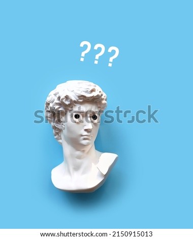 Plaster sculpture head of David with google eyes and question marks image on blue background. Gypsum copy of antique statue. creative minimal art concept. flat lay