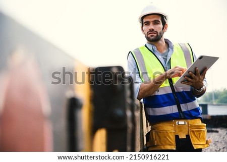 Portrait of handsome engineering using laptop for control labor worker with wear hardhat in front of train garage.  Back view of contractor on background of outdoor old train garage. Royalty-Free Stock Photo #2150916221