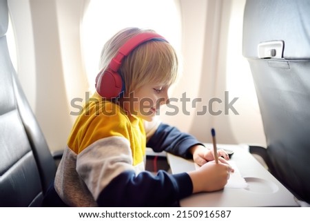 Cute little boy traveling by an airplane. Child using player to listen a music or audiobook during the flight and drawing pictures. Entertainment for family with kids on a board of plane