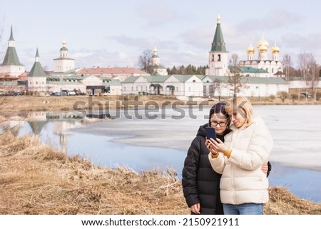 Mother and daughter take a family selfie against the backdrop of an ancient monastery and a spring landscape with a blue lake