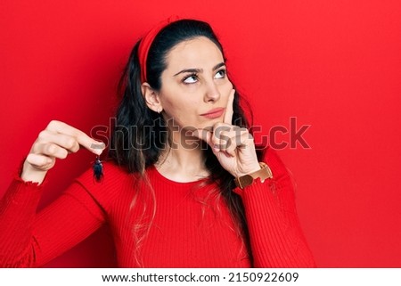 Young hispanic woman holding cockroach serious face thinking about question with hand on chin, thoughtful about confusing idea 