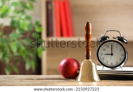 Golden school bell, apple, alarm clock and notebooks on wooden table in classroom, space for text Royalty-Free Stock Photo #2150927223