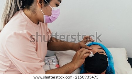 Hispanic woman wiping her patient's eyes with absorbent cotton.