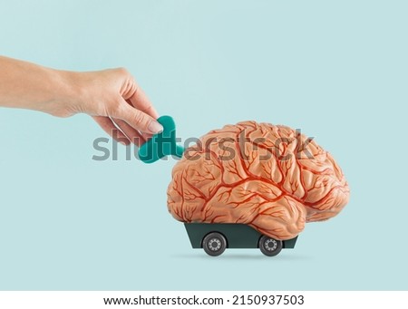 Conditioned brain. Female hand winds-up human brain. Minimal concept of brain fog, psychology treatment, influence, manipulation, persuasion or mind control. Isolated pastel blue colouring background. Royalty-Free Stock Photo #2150937503