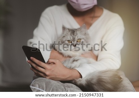 A woman uses a cell phone to a cat sitting on his lap.