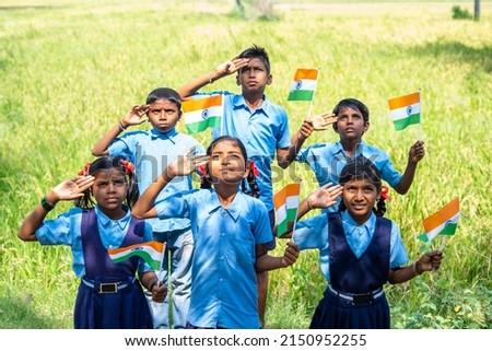 Group of village school children with Indian flag in hand saluting by looking above during flag hosting - concept of independence or republicday celebration