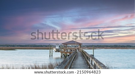 Dockside view of boathouse walking on dock with pink sky in Beaufort, South Carolina. Royalty-Free Stock Photo #2150964823