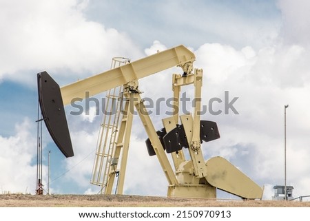 A beige and black color oil field pumpjack, or donkey, in an oil field against a cloudy sky