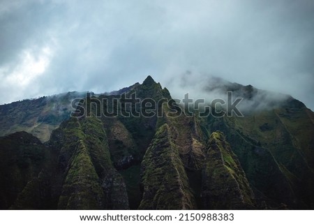 The gorgeous rugged wilderness and cliffs of Kauai's Napali Coast in Hawaii, with low clouds and mist hanging over the mountain peaks under a stormy grey sky Royalty-Free Stock Photo #2150988383