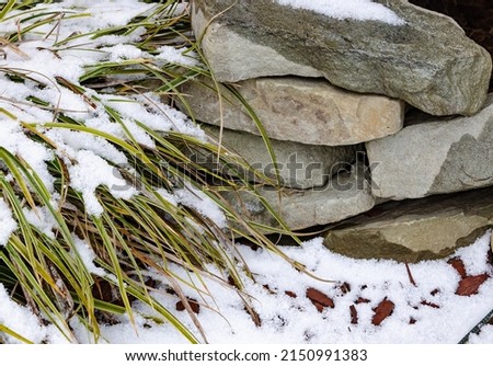 Snow on a green grass and old textured stone wall close up photo wallpaper pattern background tile 
