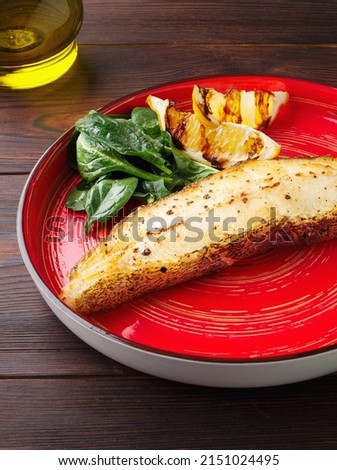 Grilled halibut steak with fresh spinach and lemon. Wooden background, red colored plate. Top view. Fish fried steak on a plate. Lunch, dinner at the restaurant. Copy space. Close up. Healthy food.