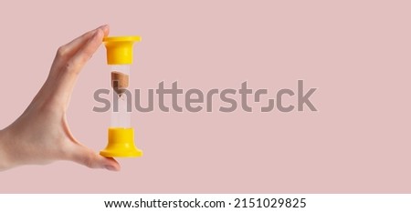 Banner with woman hand holding sand clock on pastel background. Time, punctuality concept. Device for measuring one minute passage. Space for text. High quality photo