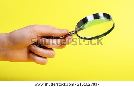 Woman hand with magnifier on yellow background. Information search, analysis and learning, audit conducting. Spy work and looking for evidence. High quality photo