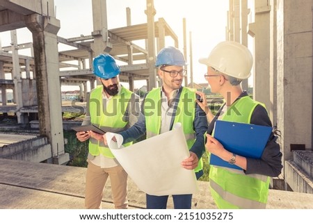 Happy mixed group of young architects looking at building blueprints and talking during meeting on a construction site Royalty-Free Stock Photo #2151035275