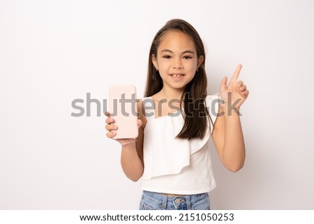 Cute beautiful little girl using smartphone pointing finger up on white background