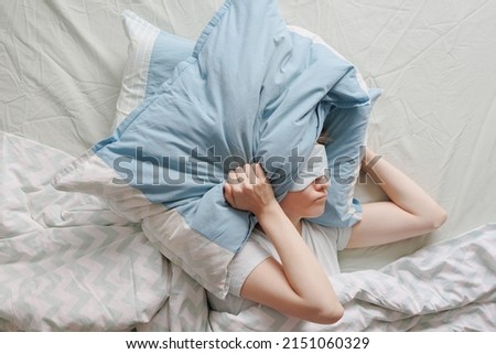 woman lies in bed and covers her head with pillows. the woman suffers from insomnia or sleep disorders. noise prevents you from sleeping at night. a tired woman can't sleep. depression and sleep Royalty-Free Stock Photo #2151060329