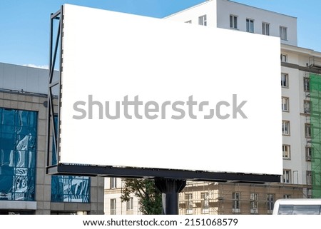 Blank white advertising billboard in front of modern buildings with glass facade in the downtown