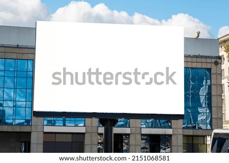 Blank white advertising billboard in front of modern buildings with glass facade in the downtown