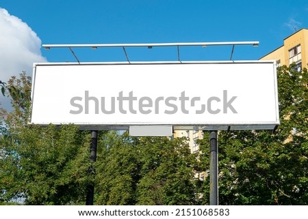 Wide billboard for advertisement in front of residential building nad trees in the city