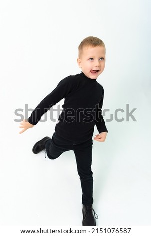 A blond boy in black clothes is showing his tongue while taking pictures in a studio