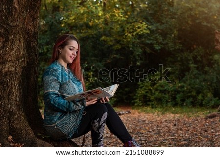 Young woman reading a book in a forest on an autumn day. Autumn day. Young woman reading. Woman in the forest. Copyspace.