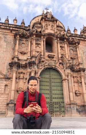 Tourist sitting in front of the cathedral looking at his cell phone in the main square of Cuzco.