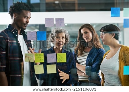 Great concepts in the making. Shot of a group of colleagues working with adhesive notes on a glass wall in the office. Royalty-Free Stock Photo #2151106091