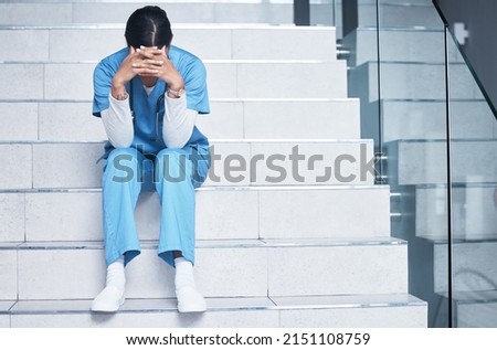 Treating sick people isnt easy and losing them is even harder. Shot of a female nurse looking stressed while sitting on a staircase. Royalty-Free Stock Photo #2151108759