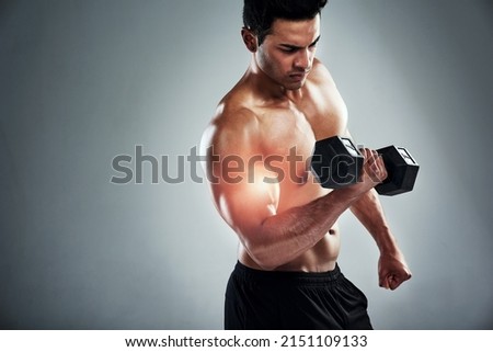 Pumping iron. Shot of a sporty young man working out with a dumbbell against a grey background.