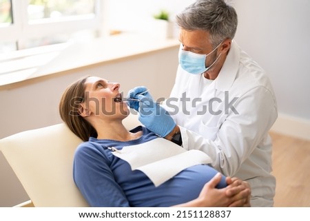 Male Dentist Treating Teeth Of Young Pregnant Woman Patient Lying In Clinic Royalty-Free Stock Photo #2151128837