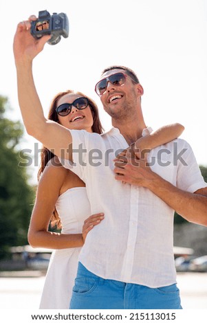 love, wedding, summer, dating and people concept - smiling couple wearing sunglasses making selfie with digital camera in park