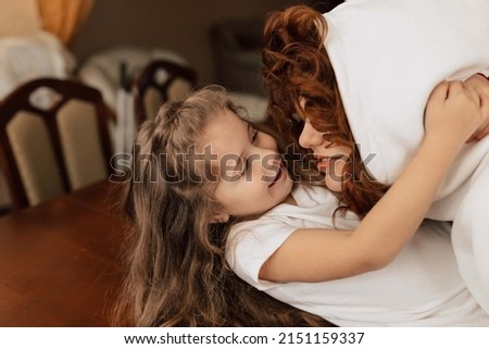 Close up indoor portrait of red haired woman in hoodie is hugging and spend time with her adorable little daughter at home. High quality photo