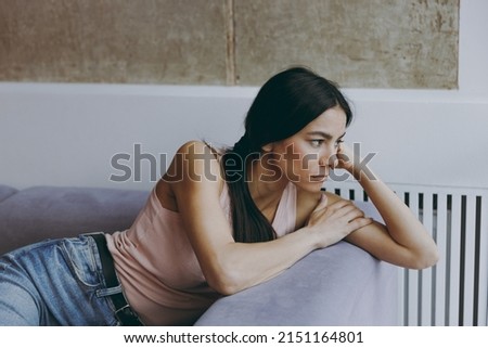 Side view profile distempered unnerved sad worried frowning minded young latin woman 20s in casual clothes sit on sofa think plan spend time in living room home in own house. People emotions concept Royalty-Free Stock Photo #2151164801