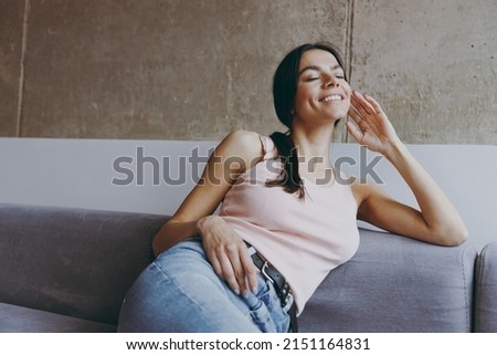 Front view smiling vivd happy fun young latin woman 20s in casual clothes eyes closed face up sit on sofa hand under cheek rest relax spend time in living room in own house be lost in reverie good day Royalty-Free Stock Photo #2151164831