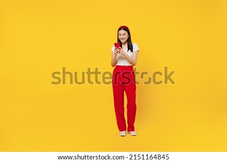 Full size body length smiling fun young girl woman of Asian ethnicity 20s years old wears casual clothes hold in hand use mobile cell phone send sms isolated on plain yellow background studio portrait Royalty-Free Stock Photo #2151164845