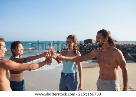 Group of joyful friends clinking glass bottles when enjoying beach party