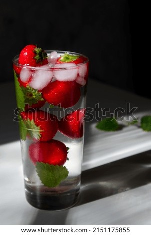 Refreshing drink with strawberries, mint and ice in hard sunlight with interesting shadows