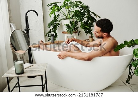 Man shaving his legs in bathroom