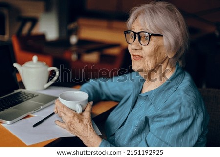 Beautiful mature senior woman with glasses sits at a table in front of a laptop Social networks unaltered